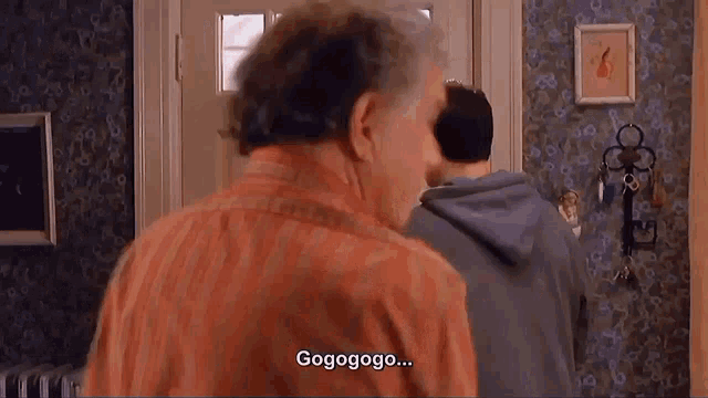 a man in a red shirt is talking to another man in a blue hoodie in a living room .
