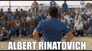 a man in a blue shirt is standing in front of a large group of men in prison .