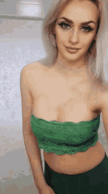 a woman is taking a selfie in a green lace top and green shorts .