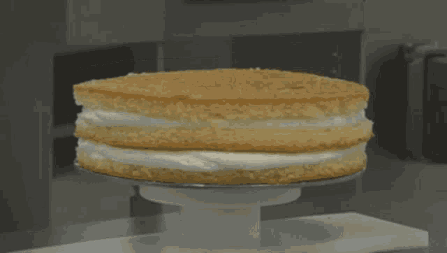 a cake is being decorated with white frosting on a white stand
