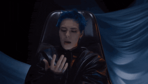 a man with blue hair is sitting in a black leather chair