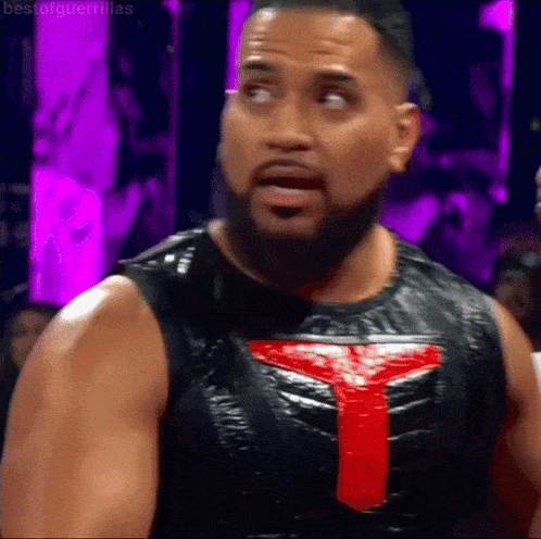 a man with a beard is wearing a black vest with a red y on the chest .