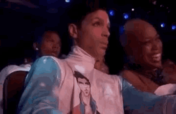 prince is wearing a t-shirt with a picture of elvis presley on it while sitting in a theatre .