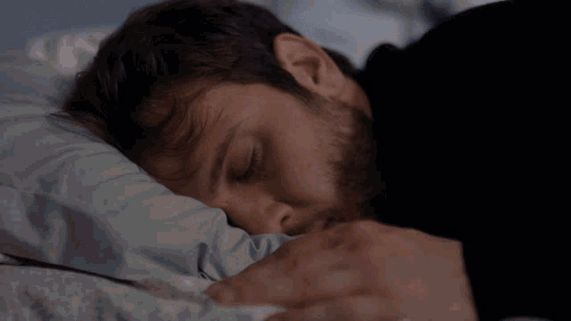 a man with a beard is sleeping on a bed with his eyes closed