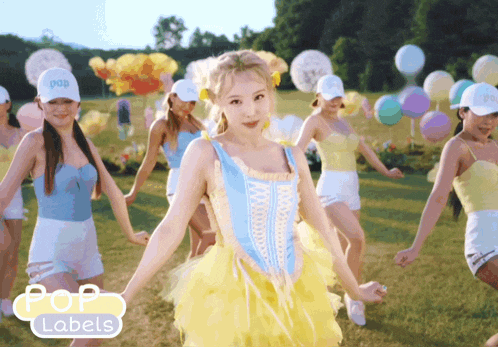 a group of women are dancing in a field with balloons in the background and pop labels on the bottom