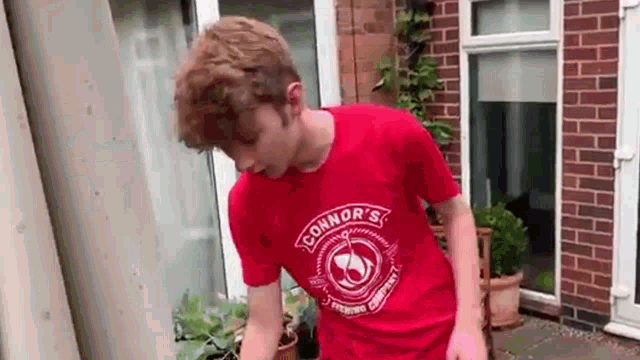 a young man wearing a red t-shirt is standing in front of a brick house .