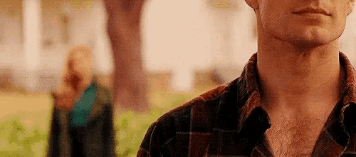 a man in a plaid shirt is standing in front of a woman in a park .