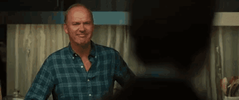a man in a blue plaid shirt is standing in a kitchen talking to another man .