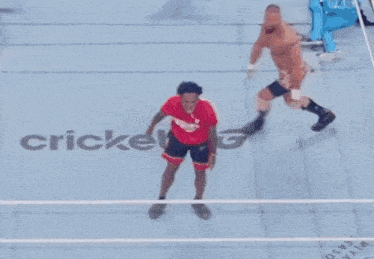 a man in a red shirt stands in a wrestling ring