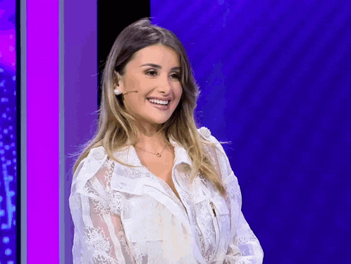 a woman wearing a white lace shirt is smiling in front of a microphone