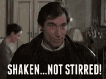 a man in a black jacket is standing in a living room with the words `` shaken ... not stirred '' written on the screen .
