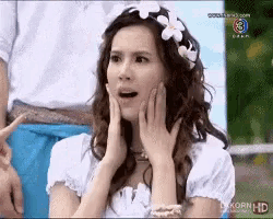 a woman in a white dress with flowers in her hair looks surprised .