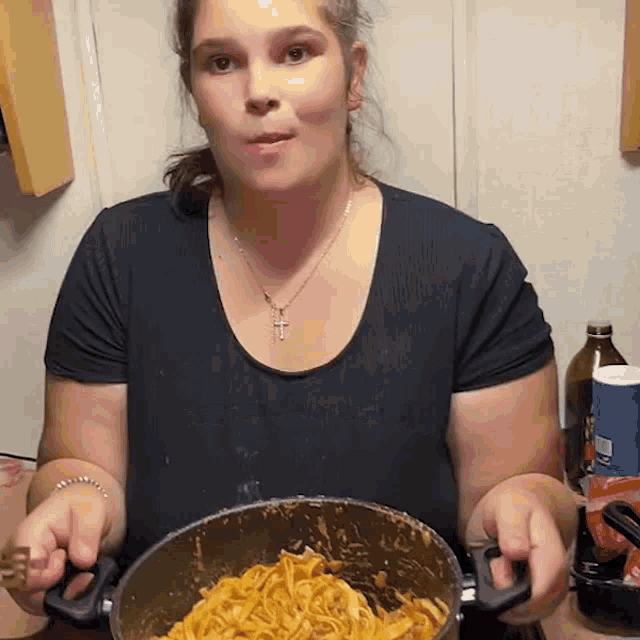 a woman wearing a cross necklace is holding a pot of noodles