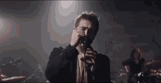 a man is singing into a microphone on a stage while a band plays in the background .