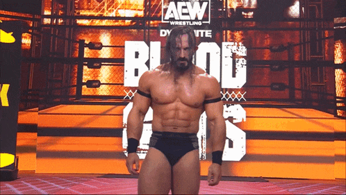 a wrestler standing in front of a sign that says aew