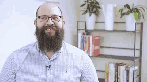 a man with a beard and glasses is smiling in front of a bookshelf filled with books .