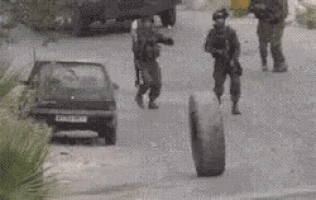 a group of soldiers are walking down a street while a car is parked on the side of the road .