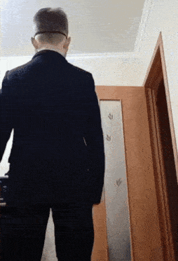 a man in a suit and glasses stands in front of a door