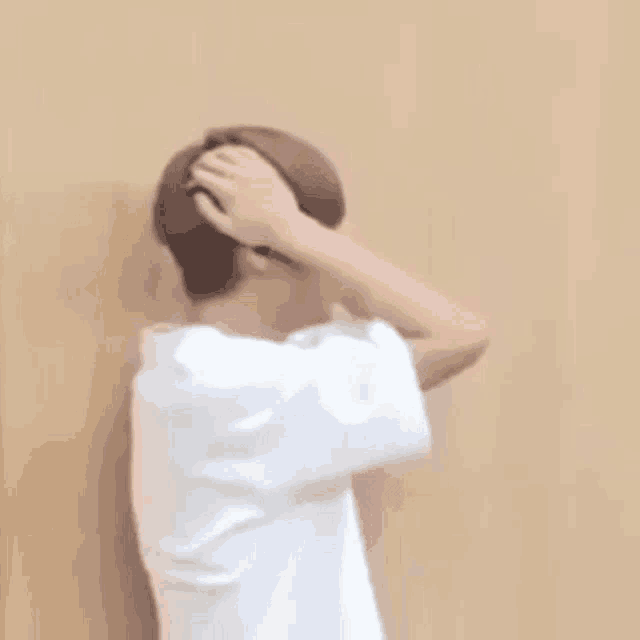 a man in a white shirt is standing in front of a wall and holding his head .