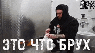 a man in a hoodie wipes his face in a public restroom with the words " это что брух " on the bottom