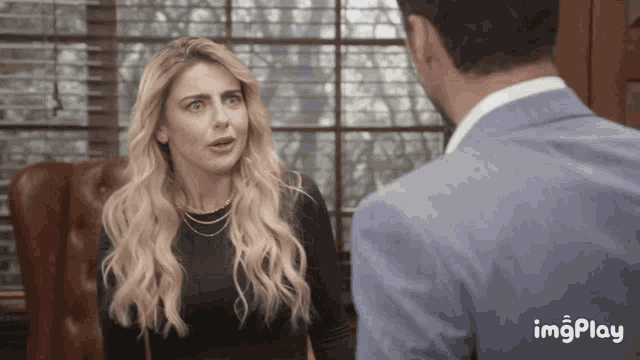 a man in a suit talks to a woman in a black top with a gif play watermark