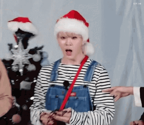a young man wearing a santa hat and overalls is holding a christmas present .