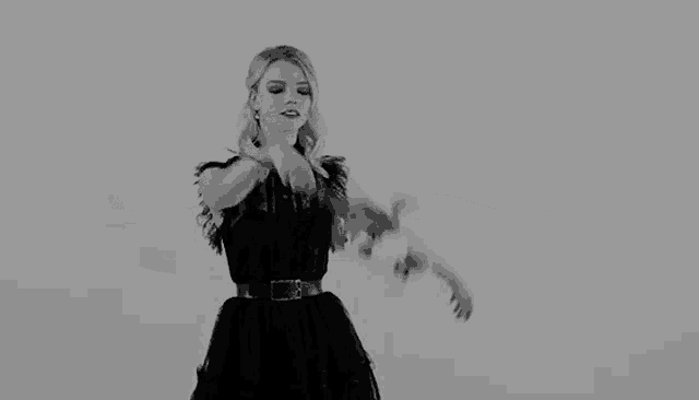 a black and white photo of a woman in a black dress holding a flower .