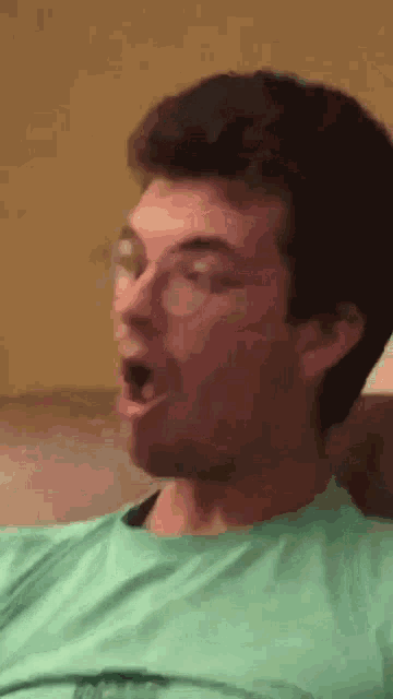 a man wearing glasses and a green shirt is making a surprised face