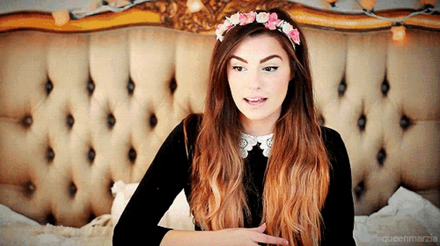 a woman with a flower crown on her head is sitting in front of a bed