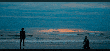 two people standing on a beach looking at a giant monster