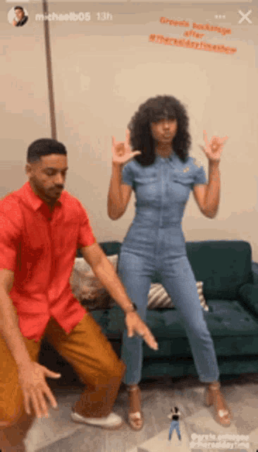 a man in a red shirt and a woman in a blue jumpsuit are dancing in front of a green couch
