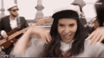 a woman in a baseball cap is dancing in front of a man playing a guitar in a band .