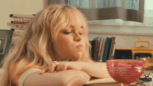 a woman with blonde hair is sitting at a table with a yellow radio and a pink bowl
