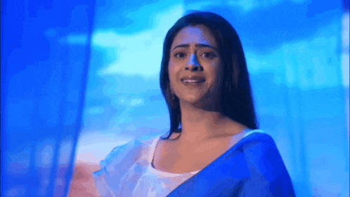 a woman in a blue saree is standing in front of a blue wall .