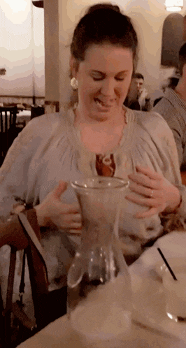 a woman is sitting at a table with a pitcher of liquid in her hands