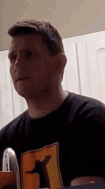 a man wearing a black t-shirt with a picture of jesus on it is sitting at a table in a kitchen .