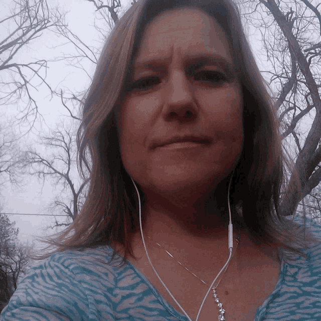 a woman wearing earbuds and a necklace looks at the camera