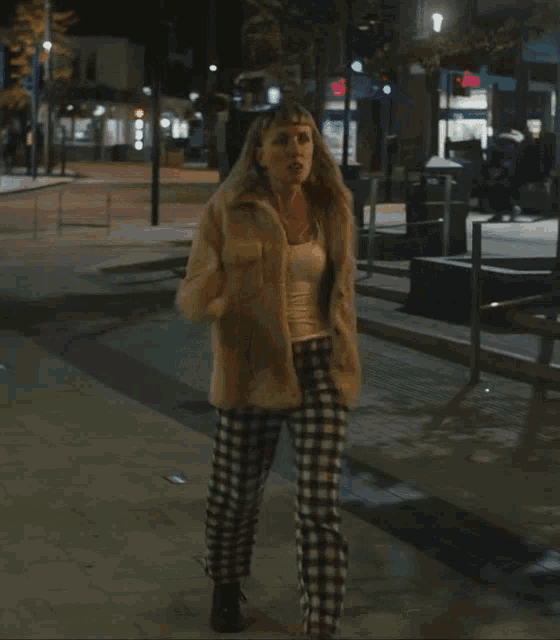 a woman wearing plaid pants and a tan jacket