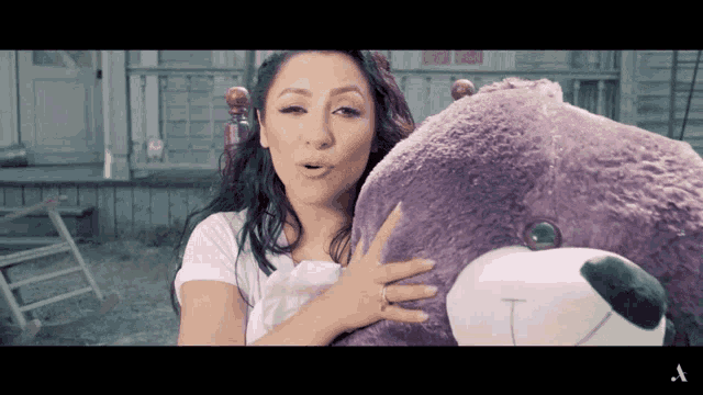 a woman holding a purple teddy bear with the letter t on its face