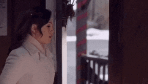 a woman in a white coat is standing in a doorway looking out the window .
