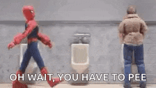 a man in a spiderman costume is walking next to another man in a urinal .