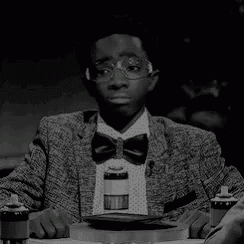 a young boy wearing glasses and a bow tie is sitting at a table with a plate of food .