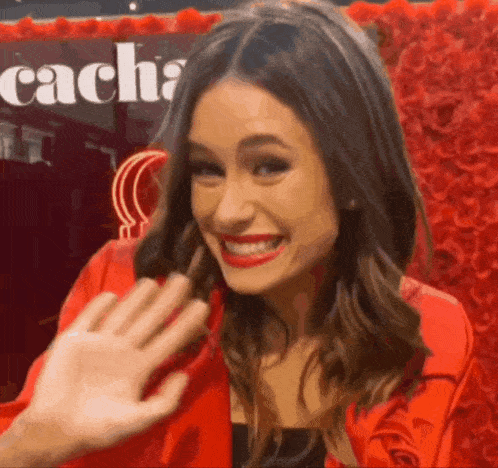 a woman in a red jacket is smiling and waving at the camera
