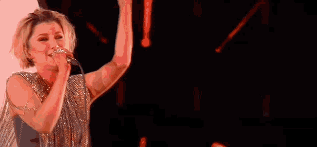 a woman is singing into a microphone with her hand in the air
