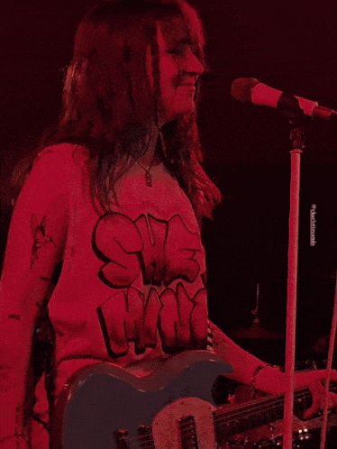 a woman singing into a microphone wearing a red shirt that says she rocks