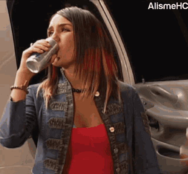 a woman in a denim jacket is drinking from a glass