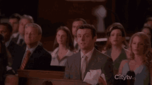 a man in a suit and tie is sitting in front of a crowd of people .