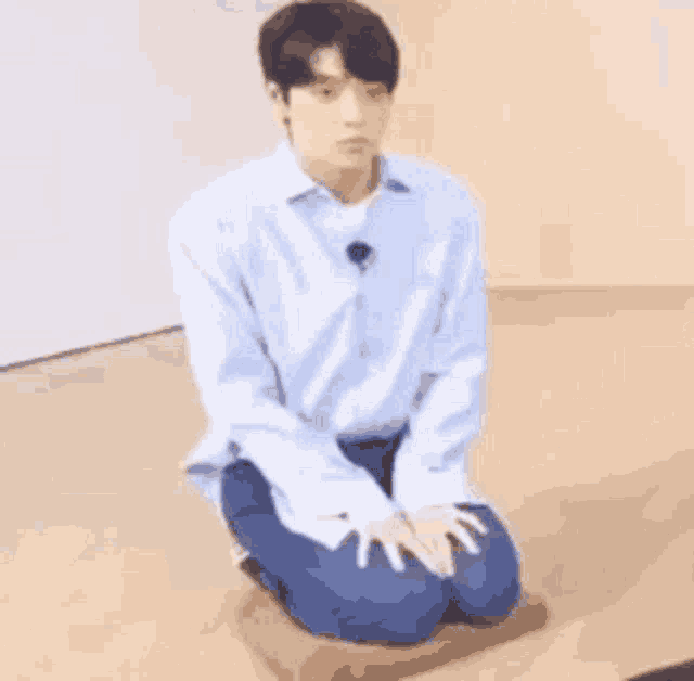 a man in a blue shirt and blue jeans is kneeling down on the floor .