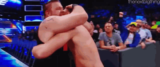 two men are hugging each other in a wrestling ring while a crowd watches .