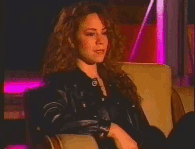 a woman in a leather jacket is sitting in a chair with her legs crossed .
